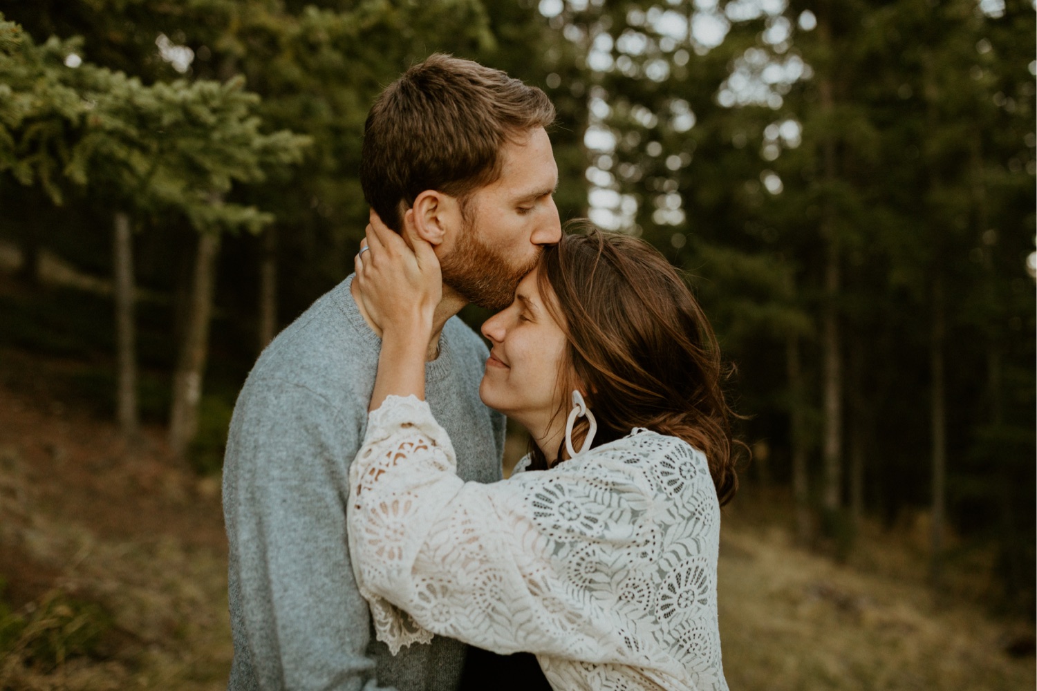 Maternity Family Photos in Calgary with mother and father dressed up for their pregnancy photoshoot with white flowy dress and baby boy in mothers belly near the mountains in Calgary Alberta during a beautiful sunset, maternity lifestyle photos in Calgary, casual lifestyle maternity photoshoot, baby photos