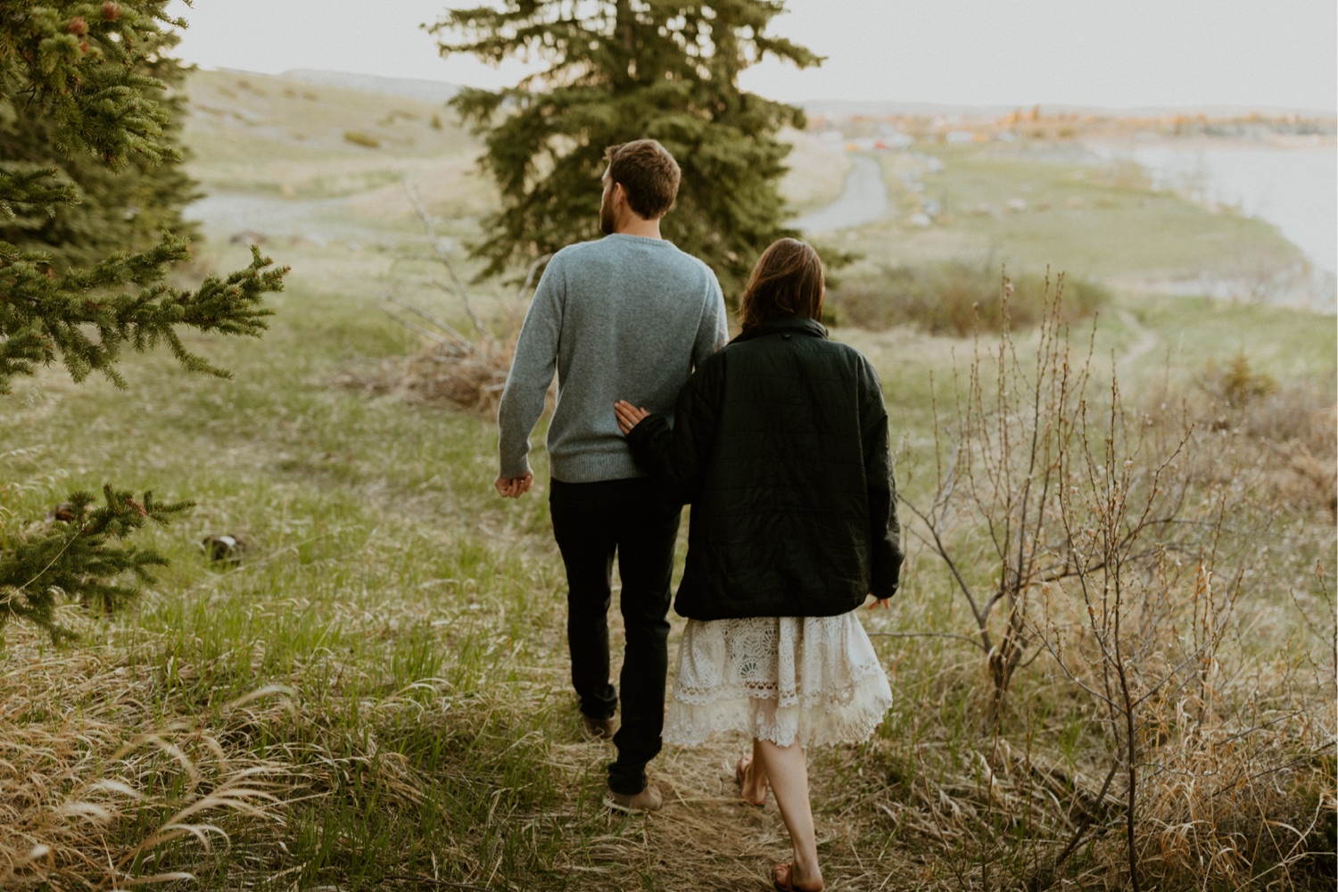 Maternity Family Photos in Calgary with mother and father dressed up for their pregnancy photoshoot with white flowy dress and baby boy in mothers belly near the mountains in Calgary Alberta during a beautiful sunset, maternity lifestyle photos in Calgary, casual lifestyle maternity photoshoot, baby photos