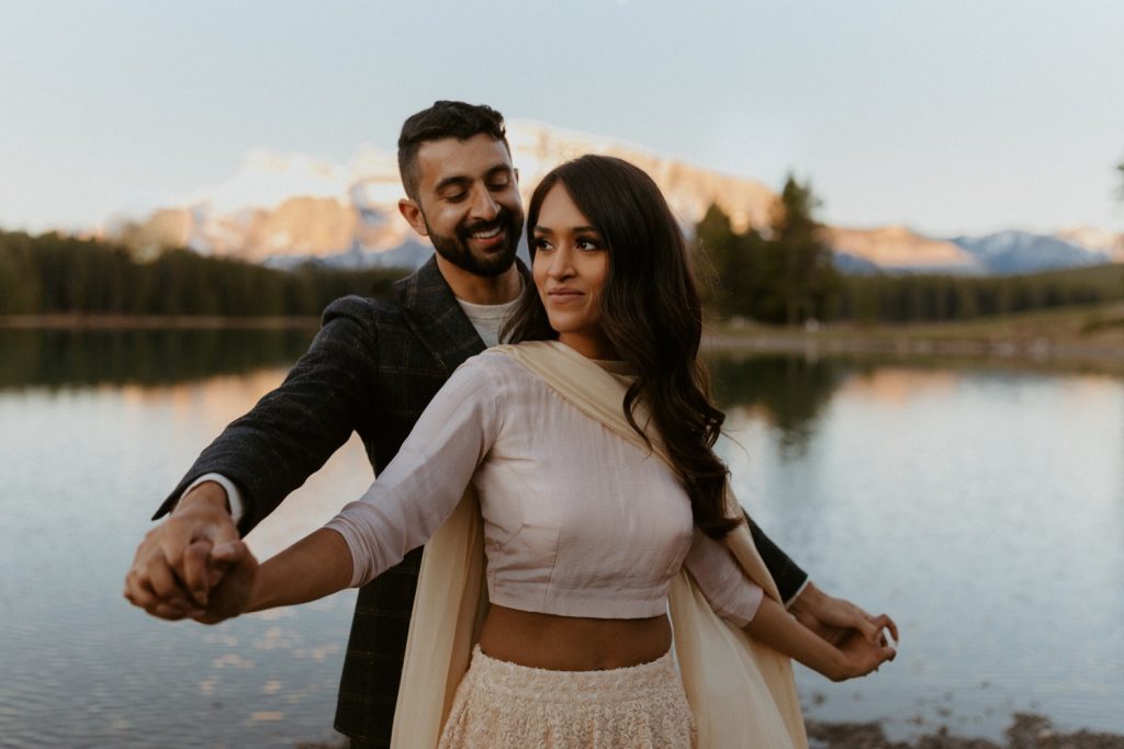 Engagement Photos in Banff at a Beautiful Lake with couple dressed up in bollywood Indian clothes for their engagement photoshoot with flowy lengha dress and suit near the mountains in Calgary Banff Alberta during a beautiful sunrise, Engagement photos, Engagement photos in Banff, Bollywood Engagement photos in Banff, Engagement photos in Banff at two jack lake